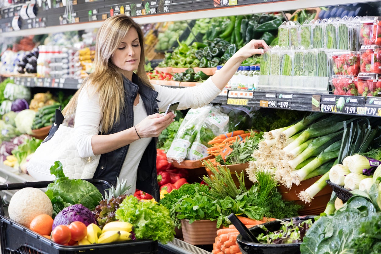 Woman with cart shopping in grocery store in the produce section. Using smart phone