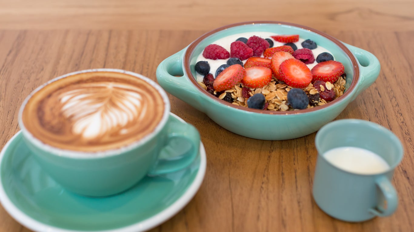 Granola Breakfast in green bowl with a glass of milk and a cup of latte coffee.