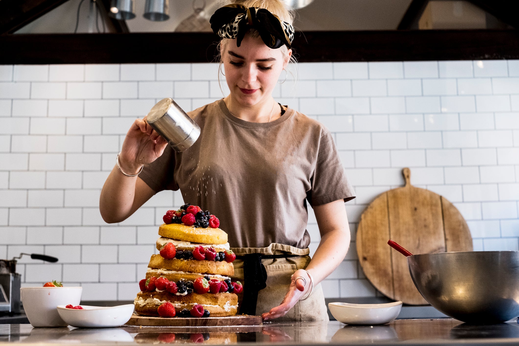 a woman sprinkles sugar on a cake which may have been baked using vegan egg substitutes