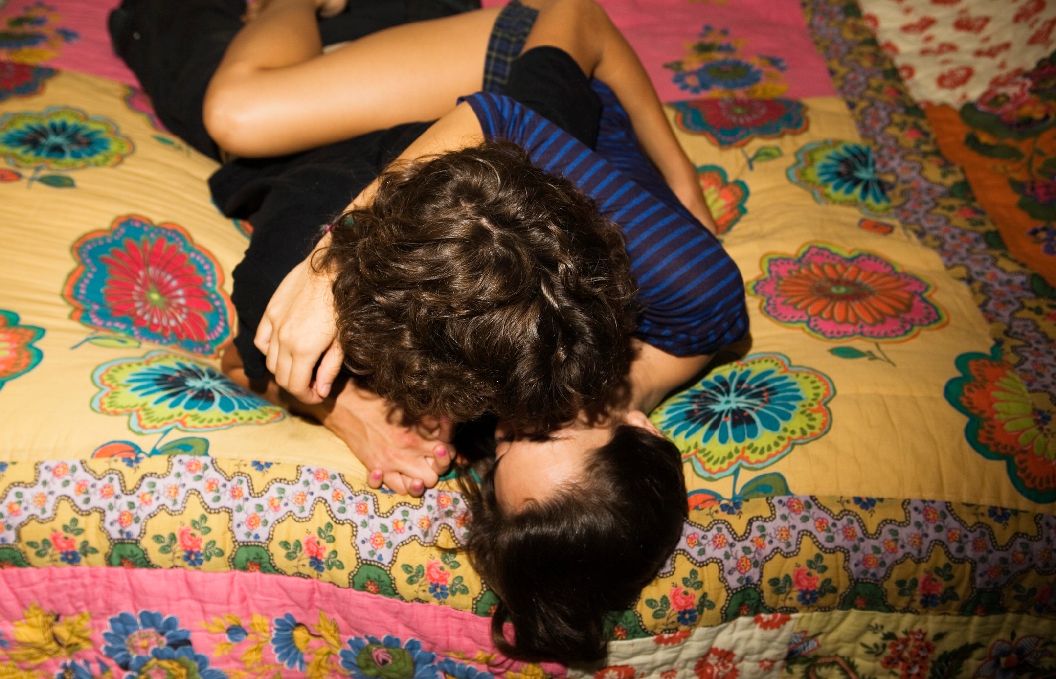 A couple embracing, kissing lying on a colorful quilt. Viwed from above.